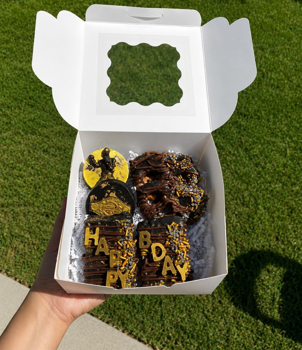 Custom chocolate-covered pretzels and treats decorated gold and black for a birthday, spelling Happy Bday