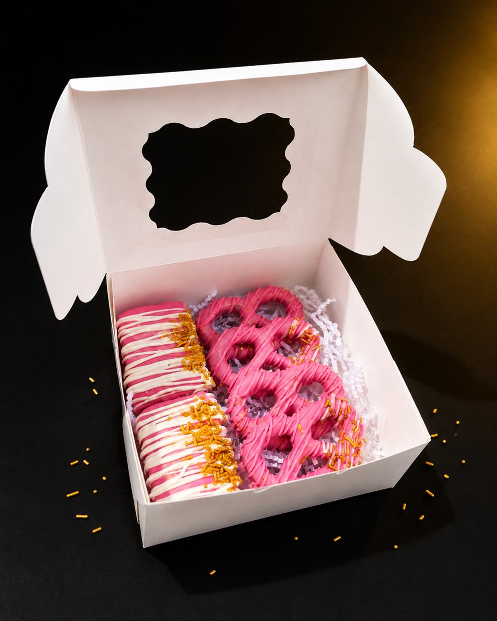 Custom pink and gold chocolate-covered pretzels and treats in a gift box